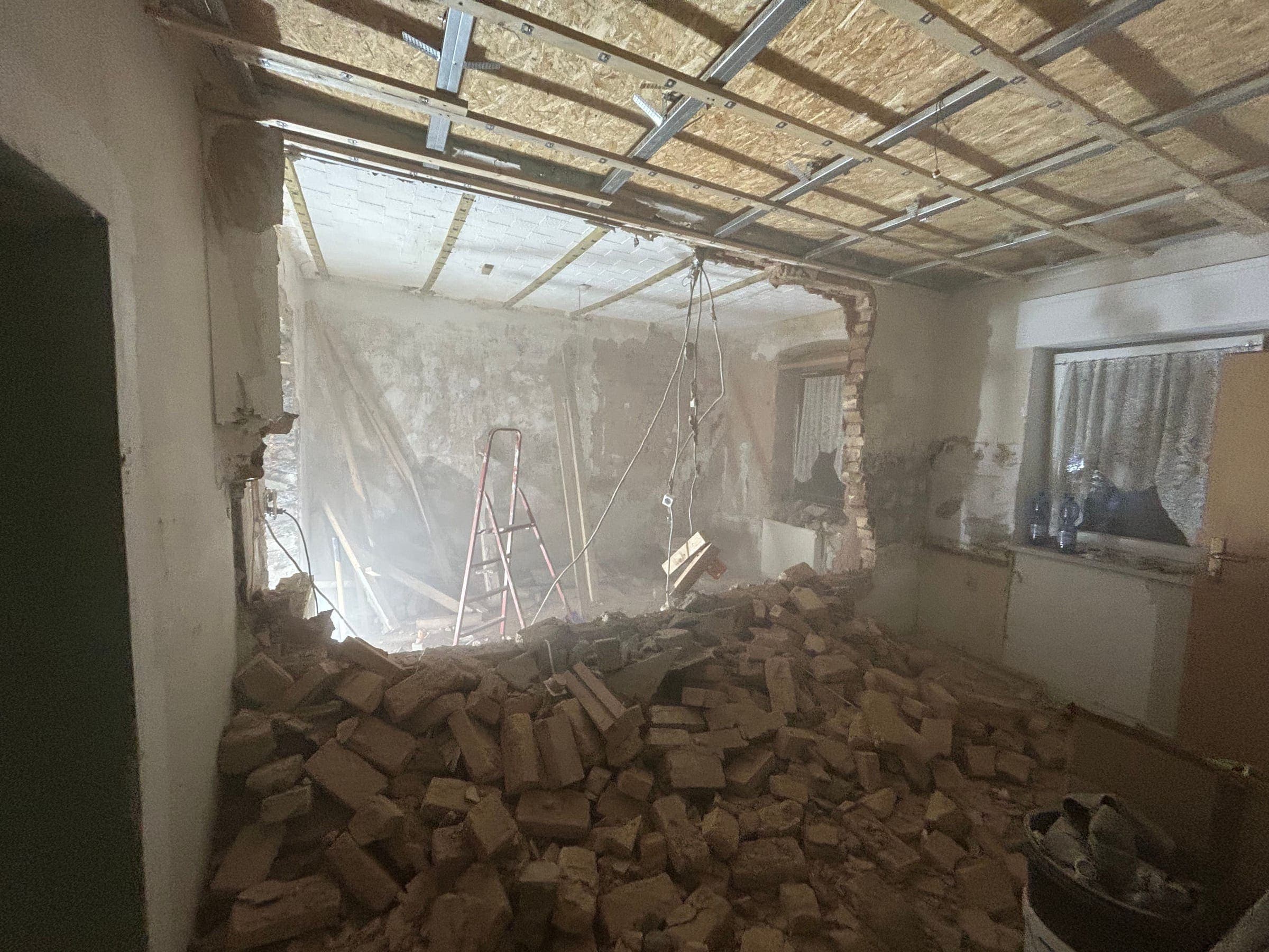 Wanddurchbruch in einer Innenwand, davor ein Haufen gelber Ziegel und Bauschutt, darüber das freiliegende Deckenraster mit Dämmung