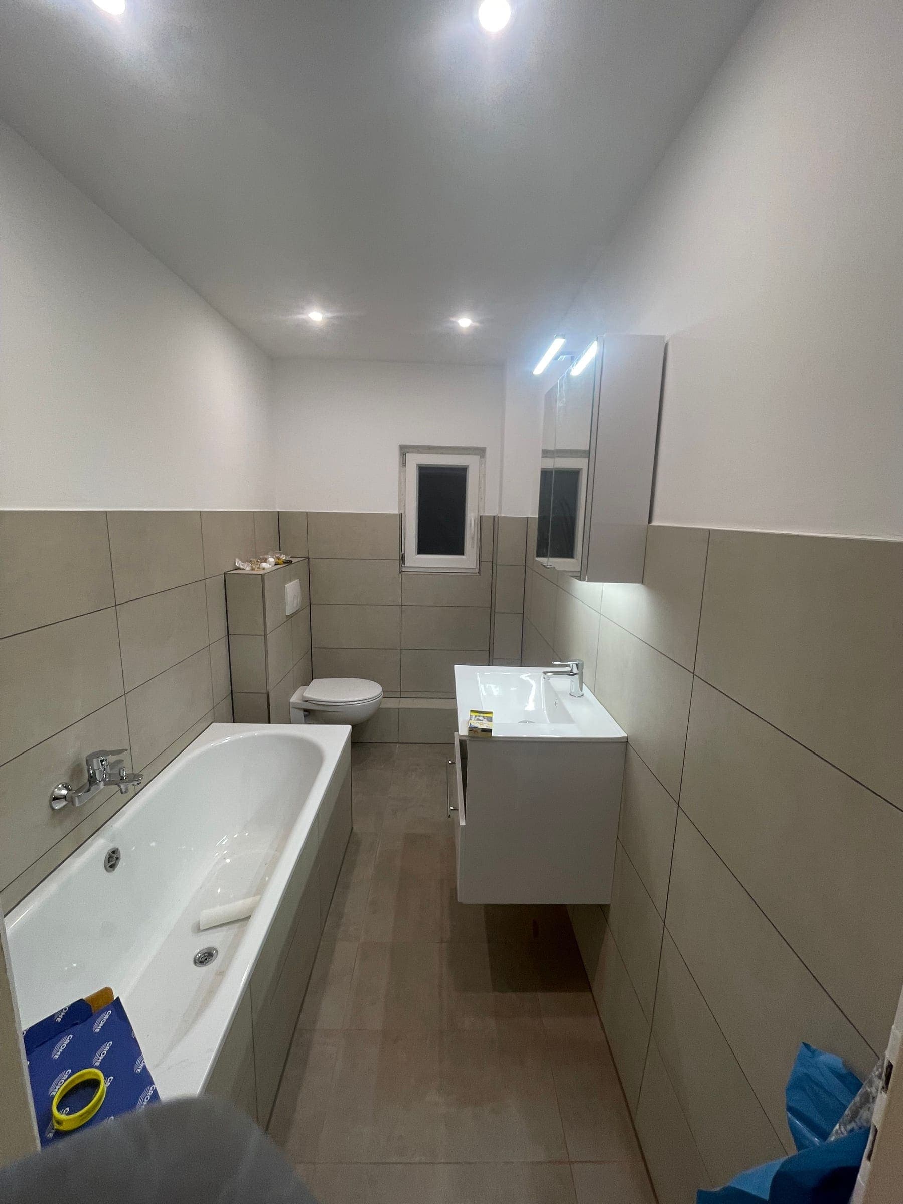 Fertiges Bad mit weißer Badewanne, beigen Großformatfliesen, Waschtisch und Spiegelschrank mit LED-Leiste